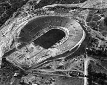 A black-and-white aerial image of a dirt field with horseshoe shaped seating around it