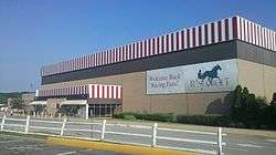 A square building with red and white vertical striping along the roof. A banner on the front shows Rosecroft's logo and the statement "Welcome Back Racing Fans!"