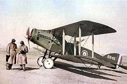 Two men in flying gear next to a military biplane