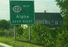 A green sign on the side of the road reading Route 122 west Alpha keep right