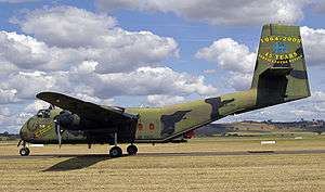 Colour photograph of an aircraft painted in a camouflage pattern taxiing along a runway