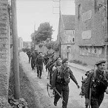 Single file of soldiers walking along a house lined street