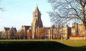 A wide shot of an old English school with a central tower, a sports pitch is seen in the foreground.