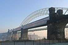 A bridge consisting of four girders on sandstone piers crossing the River Mersey seen on a frosty morning; beyond the railway bridge is the arch of the road bridge and under the arches is a church