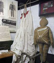 canvas figure with white parachute displayed in front of right diagrams and a medal case