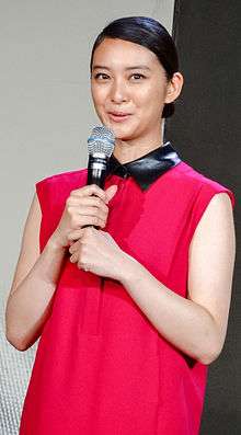 Young woman in a sleeveless red blouse, talking into a microphone