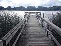 A dock that widens at the end extends out into a choppy lake on a cloudy day.