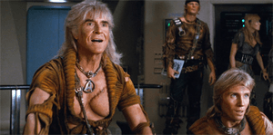 A film still showing Montalbán as Khan on the bridge of a spacecraft, wearing a torn golden shirt. His exposed chest bears a large scar, and his hair is long and grey. In the background, his followers wear similar clothes.