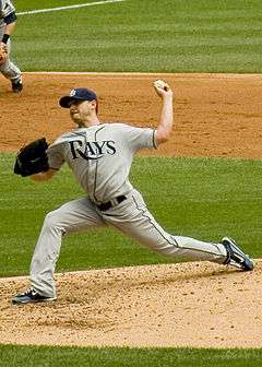 A man in a gray baseball uniform reading "Rays" across the chest throws a baseball with his left hand from a dirt mound.