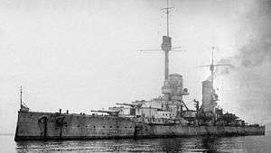 A large, light gray warship sits motionless in a calm sea