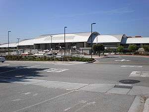 A train station with white roof situates behind an empty parking lot and road