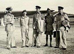 Five men in World War II military uniforms, standing on an airfield