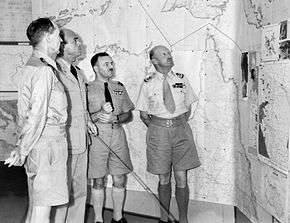 Four men in summer military uniforms in front of a map of northern Australia