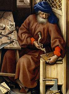 A narrow section from a wing of a large painted altarpiece. Joseph is shown as an old man in a thick brown robe and blue turban. He is seated on a tall high-backed seat with a work bench in front of him. He is drilling a piece of wood. Other tools shown on the bench and floor are a hammer and chisel, an axe, an adze, a rasp, a knife, a gimlet and a plane.
