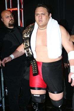 Samoa Joe holding the TNA World Heavyweight Championship belt wearing ring gear making his ring entrance