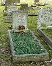 A grave covered with emerald-like gravel, with a granite headstone, surrounded by other graves