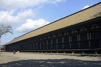 A very long wooden building with open veranda and slightly raised roof.