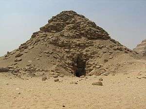 Ruined pyramid with a deep black depression at the center of the base of the pyramid.