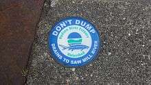 A blue and green circular medallion on a sewer warning that the discharge goes into the river
