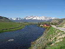 A midsized river flowing through grassland with snow-capped mountains in the background
