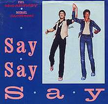 Against a blue background, "Say Say Say" is printed in pink and takes up the left and bottom of the image. To the right, there is an artwork depiction of two men holding each others' hands in the air.