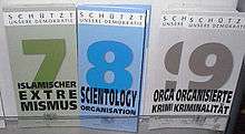 Display with three types of information leaflets, with the numbers and titles "7 Islamischer Extremismus" (coloured in shades of green), "8 Scientology Organisation" (coloured in shades of blue) and "9 Organisierte Kriminalität" (shades of grey). At the top of each leaflet is the inscription "Schützt unsere Demokratie".