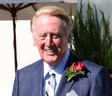 An older man, wearing a suit and a rose corsage, smiles in the sunlight.