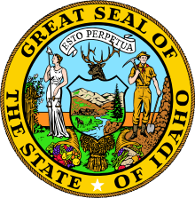 A circular seal with the text "Great Seal of the State of Idaho", along with a white star, within the outer ring. The inner ring contains a banner with the text "Esto perpetua", a woman in white holding a scale, a man dressed as a miner, and an elk's head above a shield containing a natural landscape. Below the woman and man are cornucopias, and a sheaf of grain is located under the shield.
