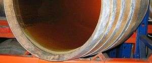 Colour photo showing the deposit of lees in barrel through a transparent bottom.  Lees looks like a layer of mud a few millimetres thick of a creamy white colour.  The light that passes through the wine is still cloudy suggesting that light should be placed against another background.  The barrel rests on metal industrial shelving.