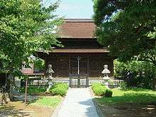 Front view of a wooden building with hip-and-gable roof and an enclosing pent roof.