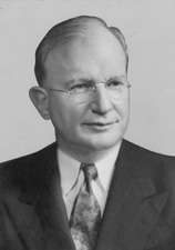 Man with thinning hair in suit and wire glasses
