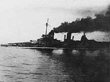 A large gray warship, heavily flooded; its deck is nearly submerged. Thick black smoke pours from the funnels. An in-photo caption reads: "Seydlitz nach der Skaggerack-schlacht", or "Seydlitz after the Skaggerak battle."