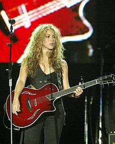 A woman standing behind a microphone, holding an electric guitar.