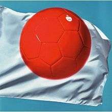 A red soccer ball against a white flag on a blue background. The ball has a small white logo of an apple.