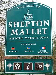 Green signs with white writing and symbols saying Welcome to Shepton Mallet, Historic Market Town, Twin Towns Misburg, Bollnas, Oissel sur Seine