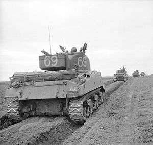 A column of tanks advance from the left to right, each tank following in the preceding tanks track marks.