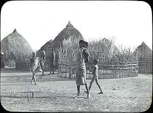 Early 20th-century village, with thatch-roofed huts and people walking
