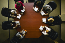 Overhead photo of eight people sitting at an octagonal table, each over an open book