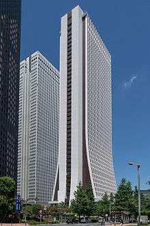 Ground-level view of a thin, brown and white high-rise; the two wider sides curve and flair out as they near the bottom