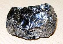 A lustrous blue grey potato-shaped lump with an irregular corrugated surface.