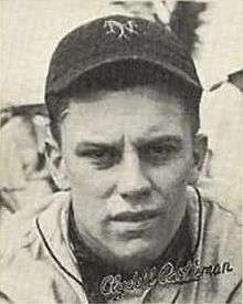 A man in a baseball uniform with a dark cap with an overlapping "NY" on the front looks into the camera.