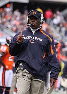 Photograph of Smith wearing a Bears pullover jacket, Bears baseball cap and headset on the Bears sideline