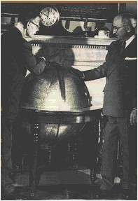 Smith (wearing glasses) and Truman lean over a large globe. A clock on the mantelpiece behind the globe indicates that it is ten o'clock.