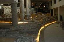 Columns and Roman brick and stone ruins on the ground floor of a hotel lit by yellow lighting