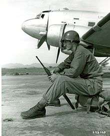 A man sits on equipment with an aircraft in the background.