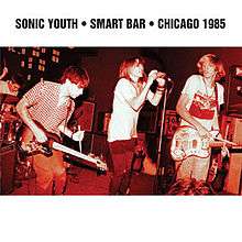 A red hue photograph of a rock band on stage. Bold black text above reads "Sonic Youth Smart Bar Chicago 1985."