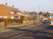 A photograph of a row of post-war housing on a main thoroughfare. The houses are a combination of semi-detached and terraced properties.