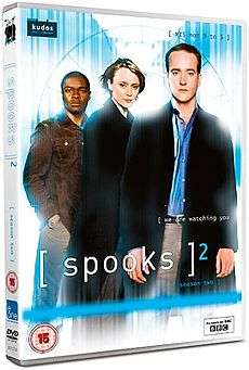 A DVD boxset cover in a light blue background with the logo "[ spooks ]2". At the top half there are three people standing. From left to right, a black British man, a short blonde-haired woman, and a Caucasian man at the front.