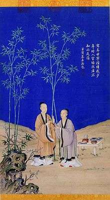 Painted vertical scroll with two men wearing robes standing on a rocky landscape and against a deep-blue sky. A strange-looking stone stands in the left foreground. There are five green bamboos in the background, and a low table with several objects on it is placed on the ground on the right. The man on the left, who is taller and looks older, is giving a long object that might be a tree branch with flowers on it to the man on the right.