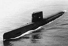 Profile shot of a long, black submarine sailing on the surface.